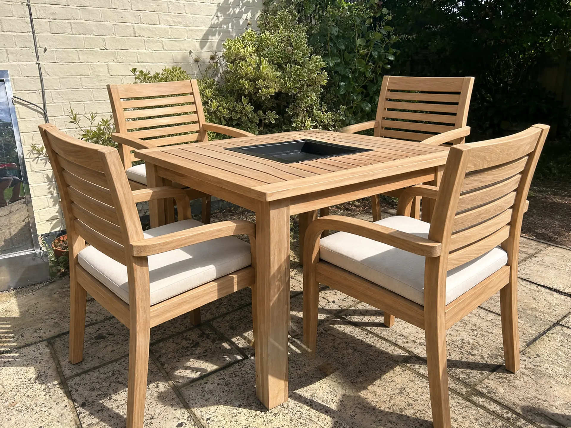Four-seat Indugia teak grill table with slatted teak chairs on a garden patio